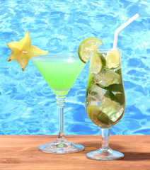 Glasses of cocktails on wooden table on blue sea background
