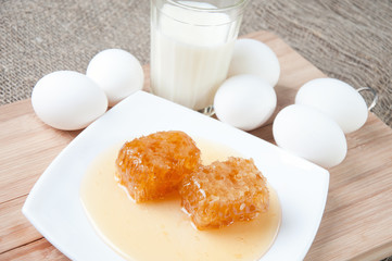 Yellow honeycomb slices on a plate, eggs and milk