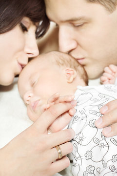 Parents holding newborn baby hand and kissing child.
