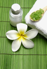 frangipani flower with massage oil and salt in spoon on towel