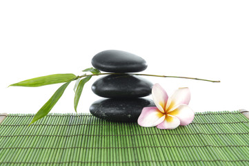 Zen stones and frangipani and a bamboo leaf on green mat