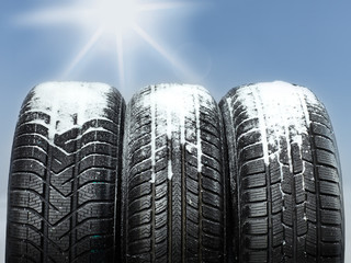 Three snowy winter tyres in front of blue sky with sunlights