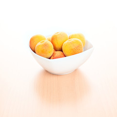 Fresh Apricots in white bowl on kitchen wooden background
