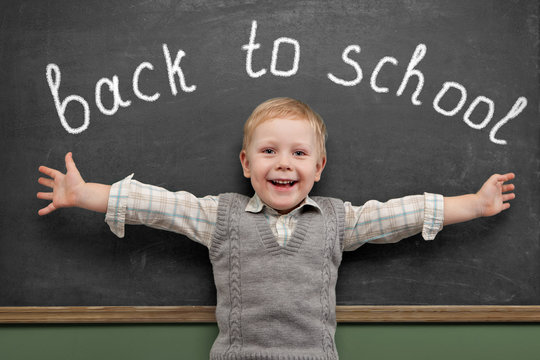 Cheerful smiling child stands at the blackboard. Looking at came