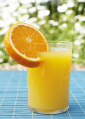 Glass of fresh orange juice against summer greens