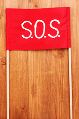 SOS signal written on red cloth on wooden background