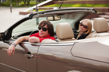 Young couple in a convertible car - obrazy, fototapety, plakaty