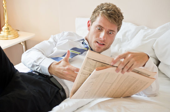 geschockter Mann mit Zeitung im Bett