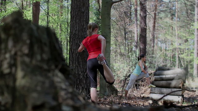 Two young women exercising and stretching in the forest