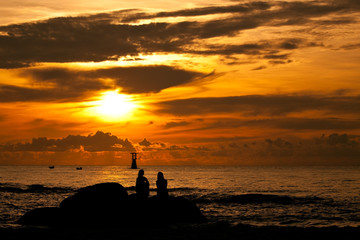 Silhouette sunrise of woman sitting on stone near by the sea