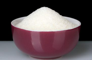 A colorful bowl full of white sugar on black background