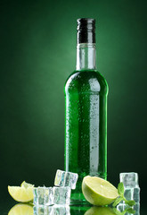 bottle of absinthe with lime and ice on green background