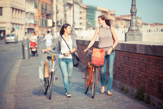 Two Beautiful Women Walking in the City with Bicycles and Bags
