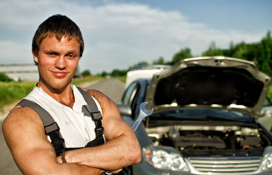 Portrait of a hadsome mechanic with a broken car on background