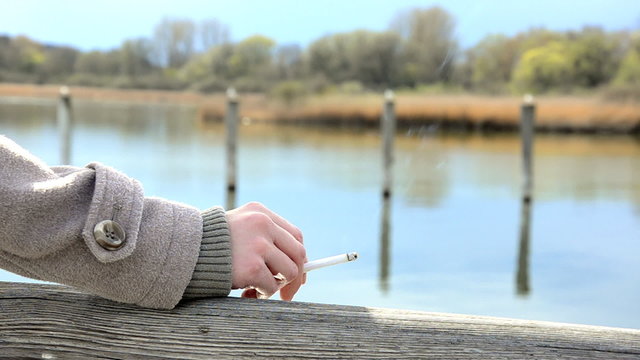 woman hold a cigarette in the backround is a lake