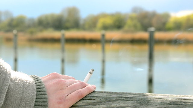 woman hold a cigarette in the backround is a lake