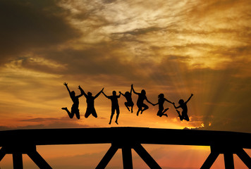 silhouette of teenagers jumping on bridge in sunset