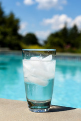 Glass of water with ice cubes on side of pool