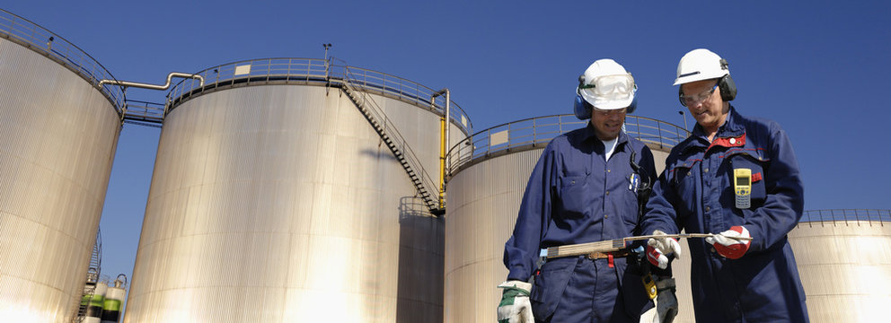 oil workers with storage towers in background