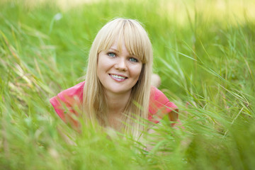 Naklejka na ściany i meble Blonde girl at green grass in the park.