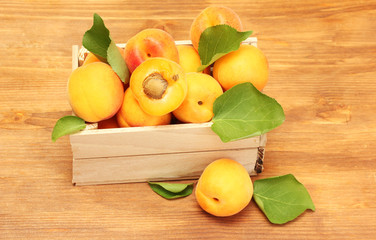 ripe apricots with green leaves in wooden box on wooden table