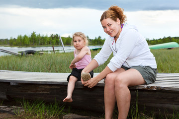 Mother helping small daughter to wear boots on river