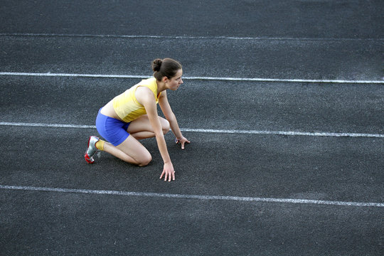 Athletic teenage girl in start position on track .