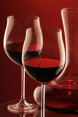 Two glasses of red wine and decanter on red background