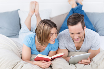 lachendes paar mit tablet-pc und buch im bett