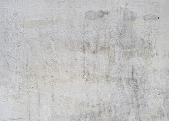 Fototapeta premium A close-up photograph of an old, dirty white concrete wall surface shows a rough grunge texture with cracked plaster and weathered stains.