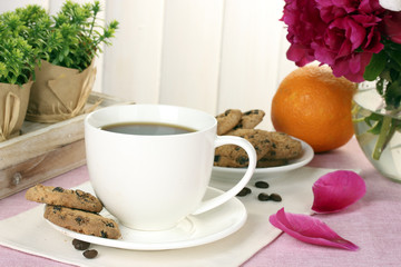 cup of coffee, cookies, orange and flowers on table in cafe