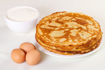 Pile of pancakes with some flour and eggs on white background