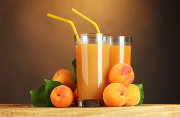 glasses of apricot juice on wooden table on brown background