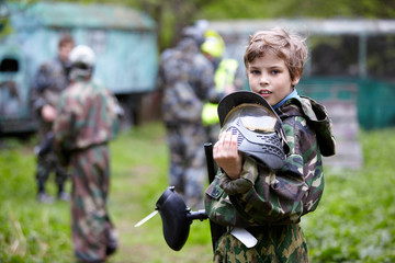 Boy in camouflage holds paintball gun barrel up in one hand - obrazy, fototapety, plakaty