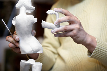 Hands of sculptor hold parts of plaster statuette.