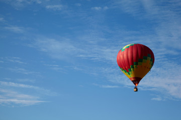 Many-colored hot air balloon with people fly in blue sky.