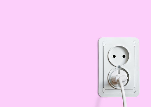 White electric socket on the pink wall .