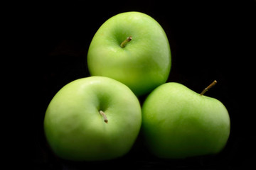 Tree green apples isolated over black background