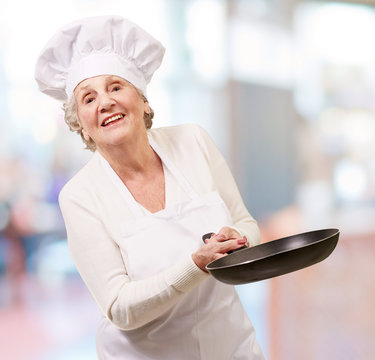 portrait of a friendly cook senior woman holding pan indoor