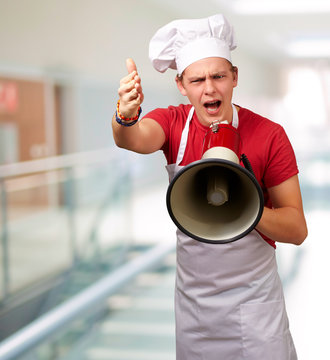 portrait of young cook man screaming with megaphone and gesturin