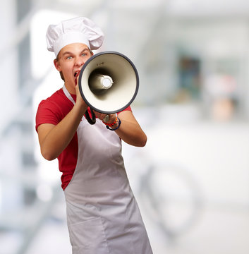 portrait of young cook man screaming with megaphone indoor
