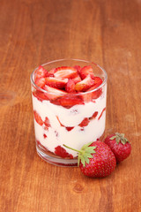 Glass of ripe strawberries with cream on wooden background