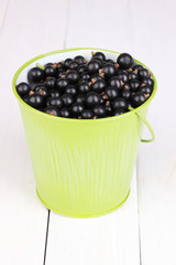Black currant in metal bucket on wooden background