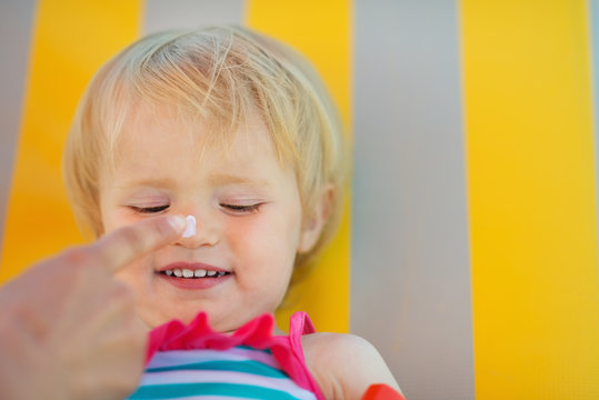 Mother's Hand Applying Sun Block Creme On Baby Nose