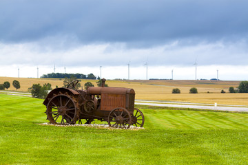Old rusty tractor with wind turbines in the background.
