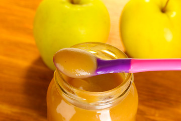 Jar with apple baby food, spoon and apples