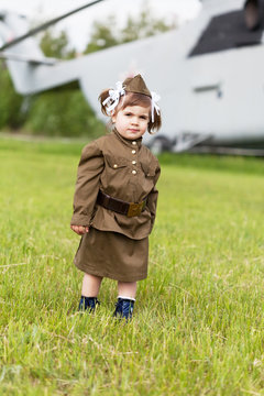 little girl in a military uniform against military planes