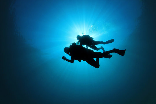 Two Scuba Divers silhouetted against sun