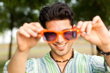 handsome man holding a pair of orange sunglasses and smiling