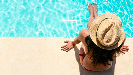 Woman sitting in a swimming pool with a sunhat - obrazy, fototapety, plakaty
